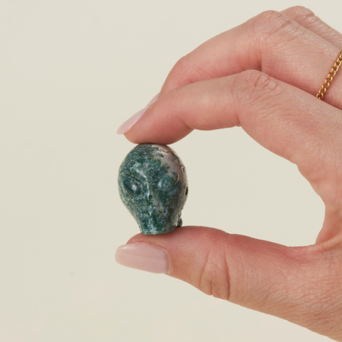 a woman's hand holding a wholesale moss agate crystal alien skull.