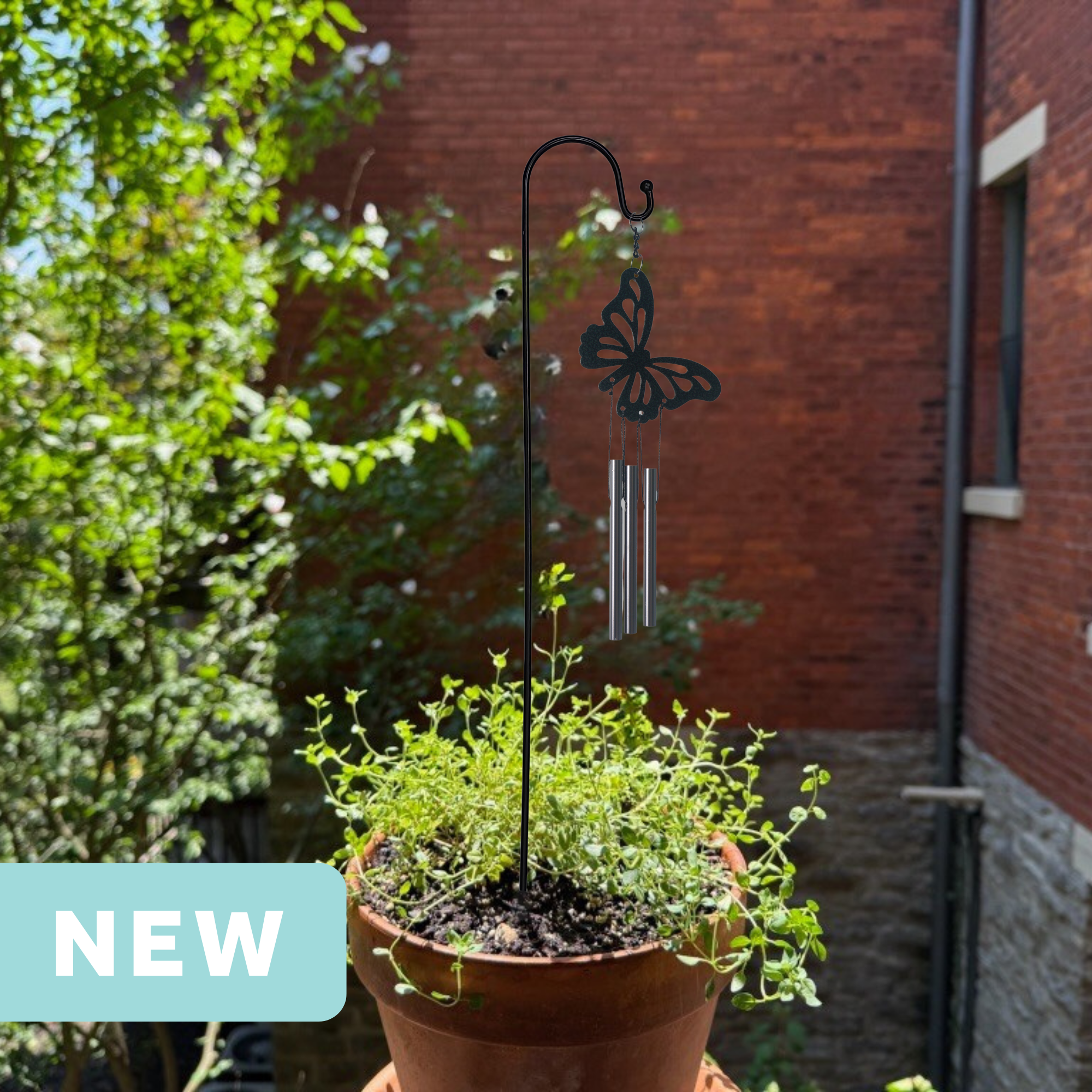 butterfly mini wind chime in a plant pot on an apartment balcony facing a brick wall