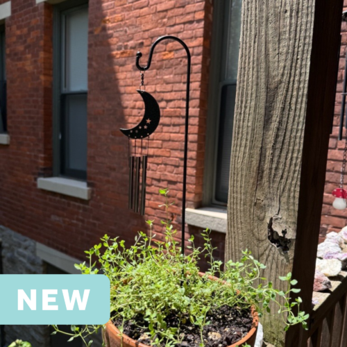 crescent moon mini wind chime in a plant pot on an apartment balcony facing a brick wall