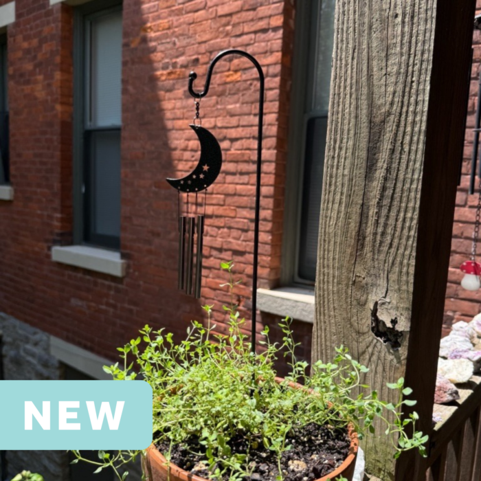 crescent moon mini wind chime in a plant pot on an apartment balcony facing a brick wall