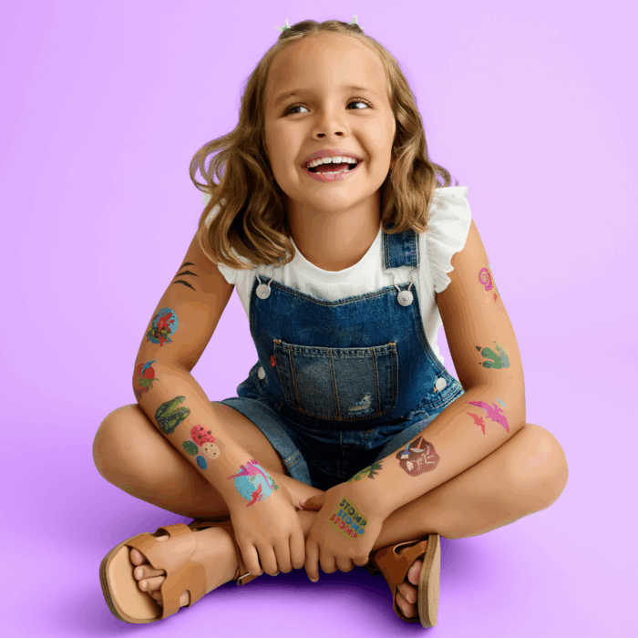 smiling child with wholesale temporary tattoos on both arms: smiling child wearing wholesale dinosaur themed kids temporary tattoos - pterodactyl, t-rex, brachiosaurus, Styracosaurus, stegosaurus, fossils, volcanoes, footprints, flora and fauna