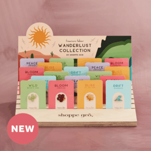 5 wholesale mini carved crystals mounted on backer cards - carnelian hibiscus, nephrite jade cactus, amazonite wave, amethyst mountain, yellow jade sun on a wooden card display with a backer card that reads Treasure Tokens Wanderlust Collection on a mauve background with a pink badge that says NEW