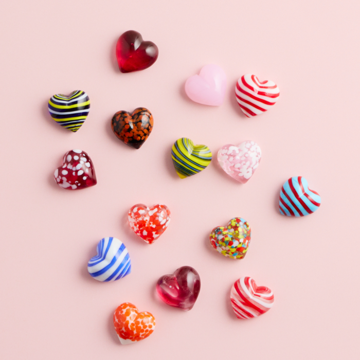 wholesale artisan glass hearts on a pink background. hearts are multicolored with various patterns.