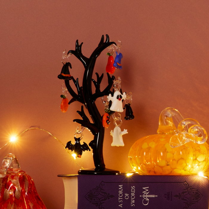wholesale glass halloween tree with halloween themed ornaments - pumpkins, witch hats, ghosts, and a bat. this is shown on top of a purple book on a mantle decorated for halloween next to glass pumpkins