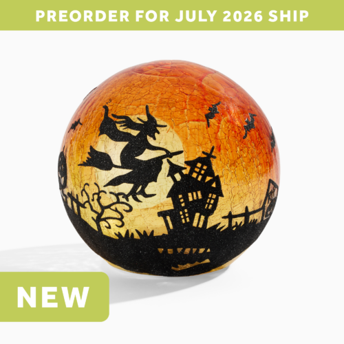 wholesale crackle glass LED lantern showing the black silhouette of a witch on a broomstick flying over a landscape featuring a whimsical crooked haunted house, crooked trees, and bats flying around her. The background is dark orange crackle glass and shows a light orange full moon behind the witch. text on the image says: preorder for july 2026 ship. NEW,