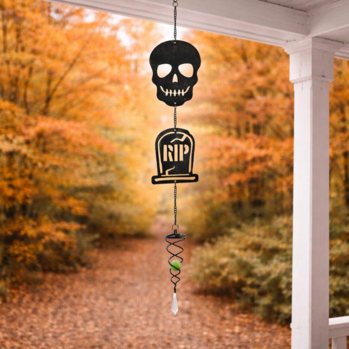 wholesale glow in the dark hanging garden wind spinner featuring a skull and tombstone that shows the letters RIP. this is hanging on a porch facing a forest with orange leaves